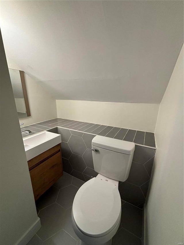 bathroom with toilet, tile patterned flooring, vaulted ceiling, vanity, and tile walls