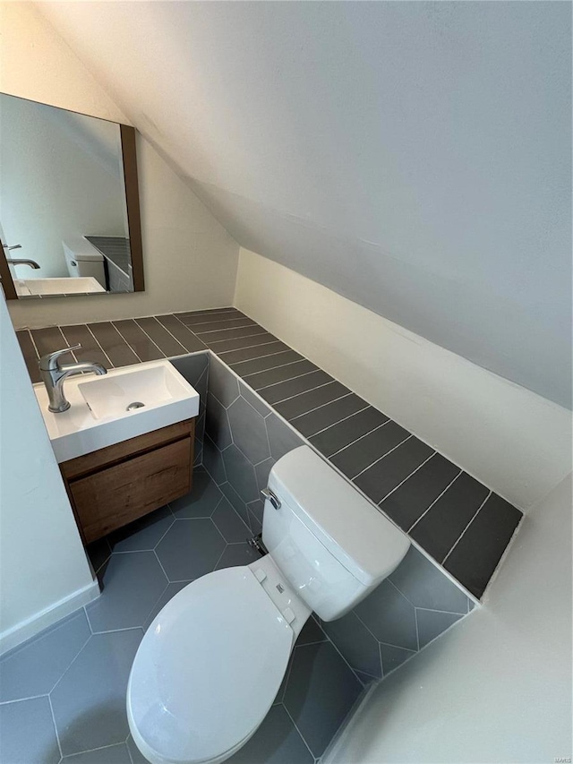 half bathroom with vaulted ceiling, vanity, toilet, and tile walls