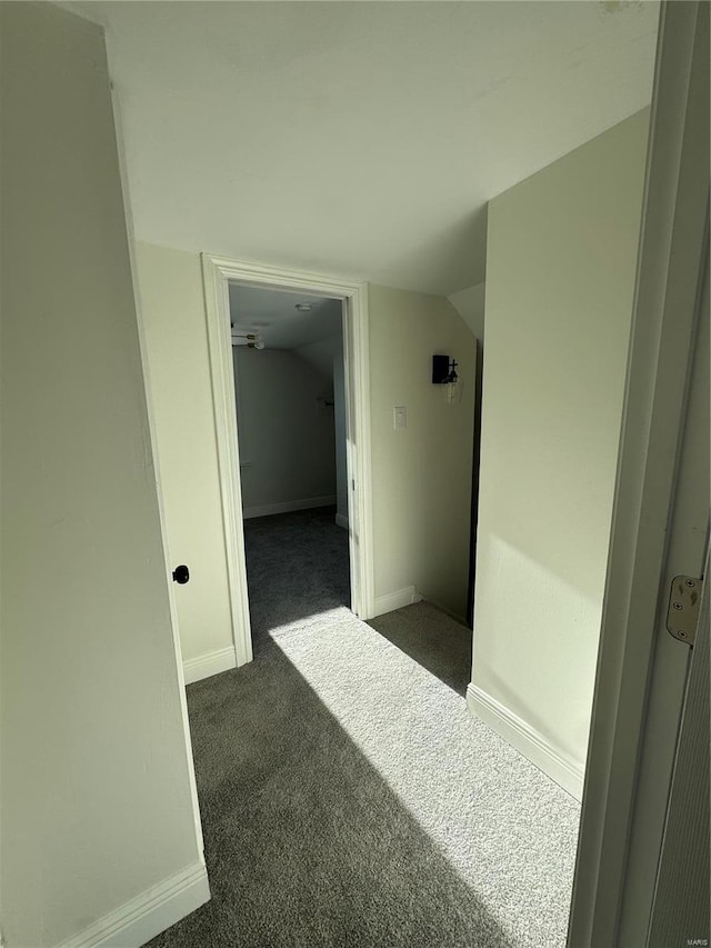 corridor featuring vaulted ceiling, baseboards, and dark colored carpet