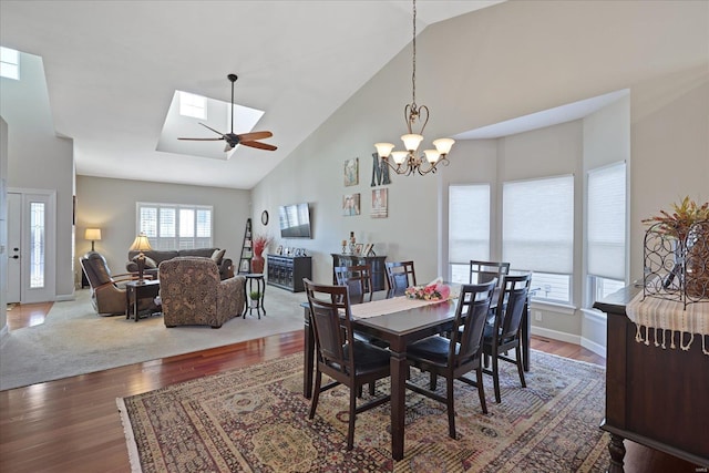 dining room with a skylight, wood finished floors, high vaulted ceiling, baseboards, and ceiling fan with notable chandelier