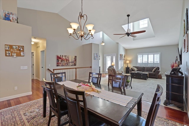 dining space with a skylight, baseboards, wood finished floors, high vaulted ceiling, and ceiling fan with notable chandelier