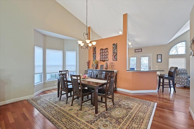 dining room featuring a notable chandelier, high vaulted ceiling, wood-type flooring, and baseboards