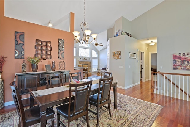 dining area featuring high vaulted ceiling, a fireplace, wood finished floors, and baseboards