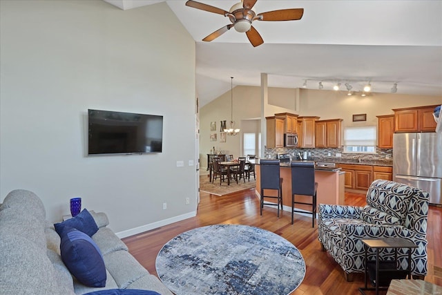 living room featuring ceiling fan with notable chandelier, high vaulted ceiling, wood finished floors, and baseboards