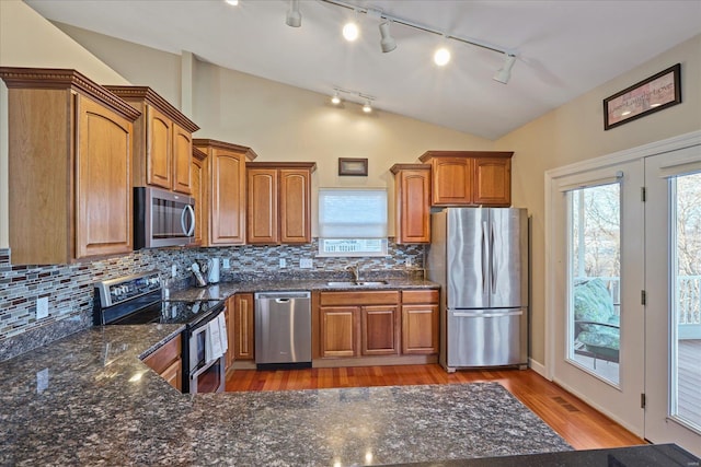 kitchen with stainless steel appliances, a sink, a healthy amount of sunlight, vaulted ceiling, and brown cabinetry