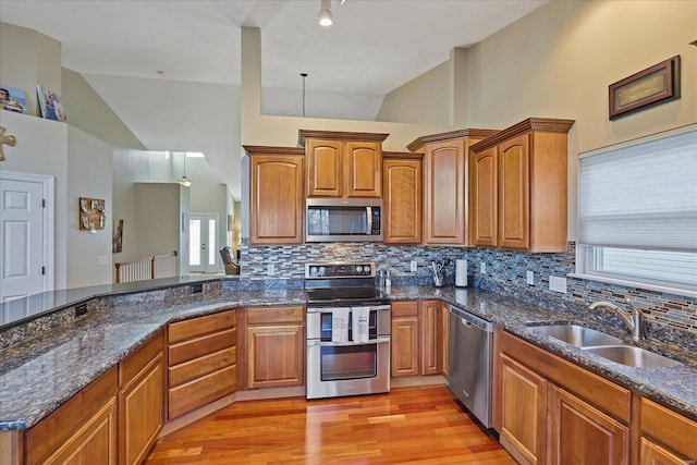 kitchen featuring brown cabinets, appliances with stainless steel finishes, light wood-style floors, a sink, and dark stone counters