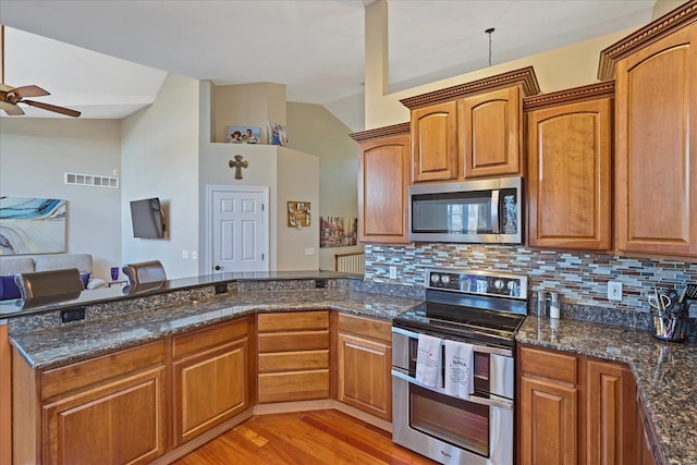 kitchen with a peninsula, open floor plan, appliances with stainless steel finishes, light wood-type flooring, and dark stone countertops