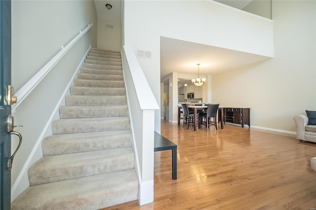 staircase featuring baseboards, visible vents, a towering ceiling, wood finished floors, and an inviting chandelier