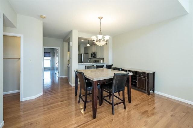 dining space with baseboards, a chandelier, and light wood-style floors