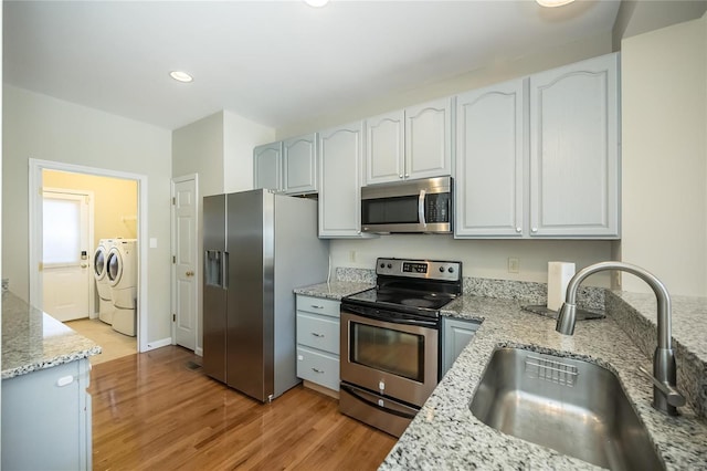 kitchen featuring washing machine and clothes dryer, appliances with stainless steel finishes, light wood-style floors, a sink, and light stone countertops