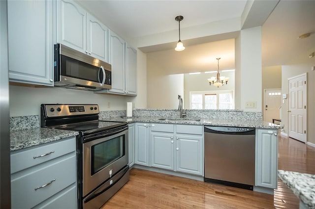 kitchen featuring pendant lighting, stainless steel appliances, light wood-style floors, a sink, and light stone countertops