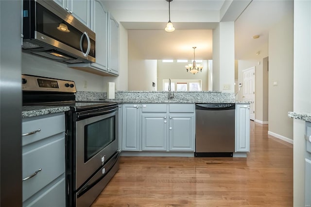 kitchen featuring light wood finished floors, appliances with stainless steel finishes, light stone countertops, pendant lighting, and a sink