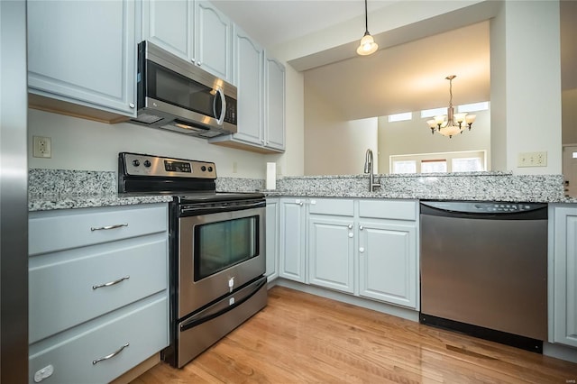 kitchen with appliances with stainless steel finishes, hanging light fixtures, light stone countertops, an inviting chandelier, and light wood-style floors