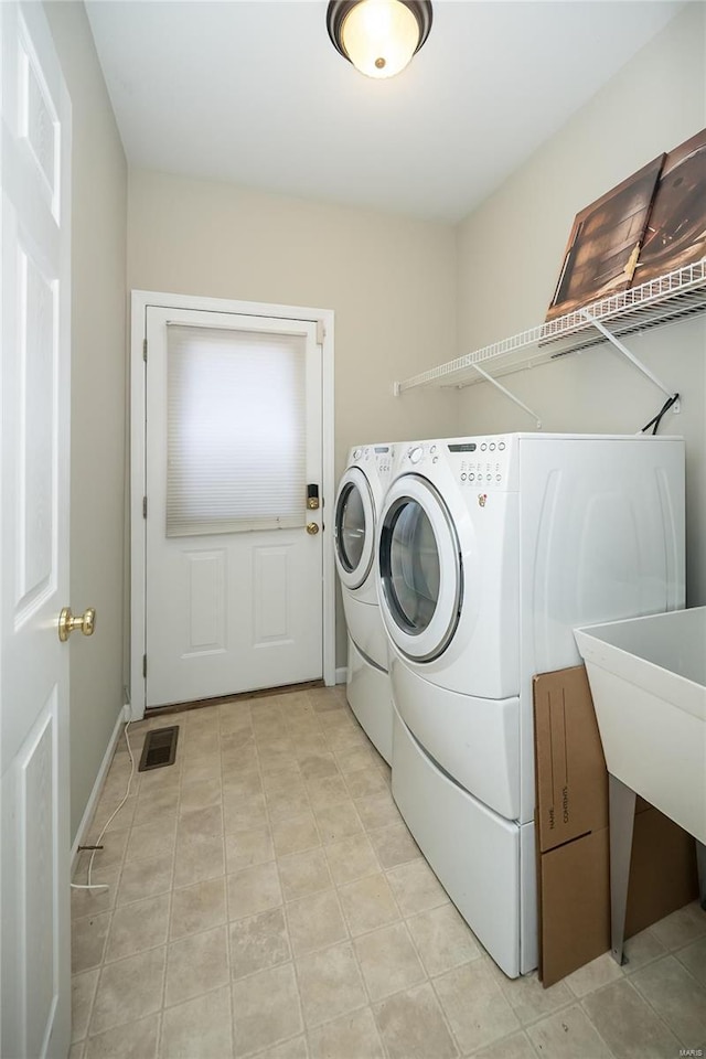 clothes washing area with washing machine and clothes dryer, visible vents, a sink, laundry area, and baseboards