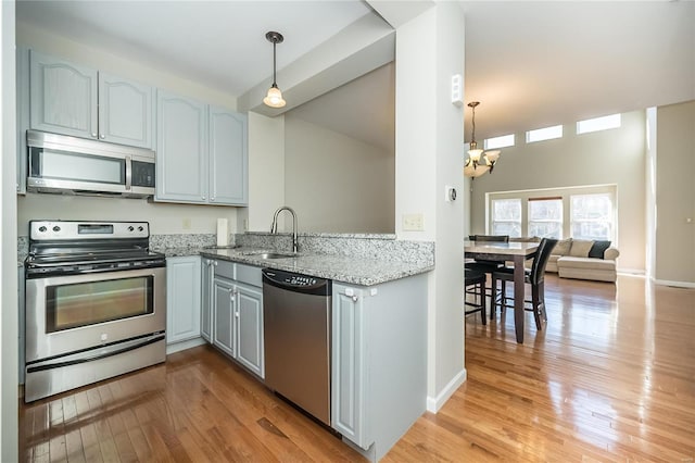 kitchen featuring light stone counters, an inviting chandelier, stainless steel appliances, light wood-type flooring, and a sink