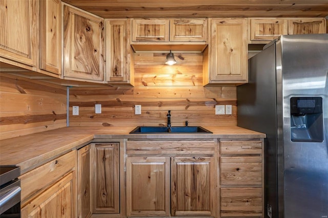 kitchen featuring stove, stainless steel refrigerator with ice dispenser, a sink, and light brown cabinetry