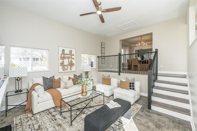 living area with ceiling fan with notable chandelier, stairway, and baseboards