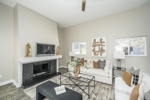 living room with a brick fireplace, ceiling fan, and baseboards