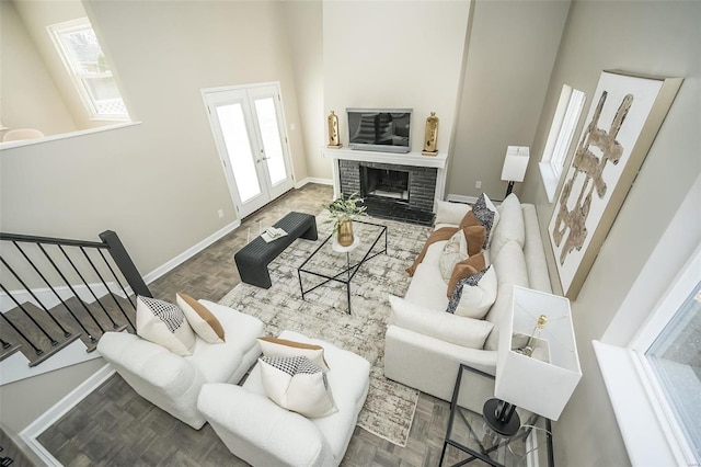 living room with french doors, a brick fireplace, a towering ceiling, and baseboards