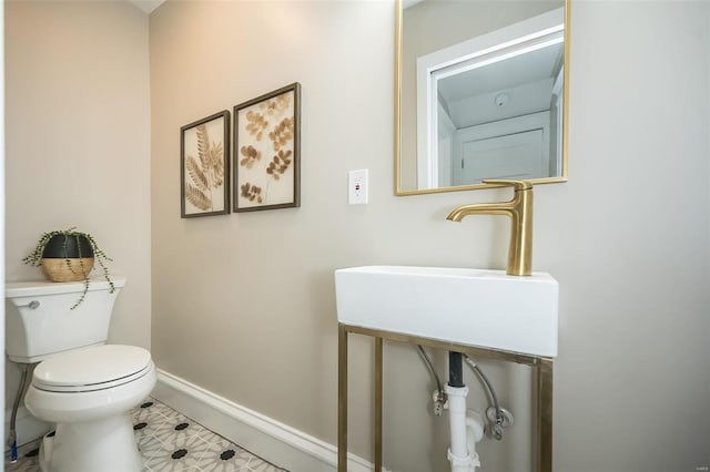 half bathroom with baseboards, a sink, and toilet