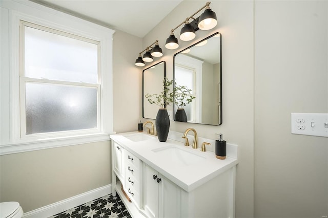 bathroom with toilet, a sink, baseboards, and double vanity