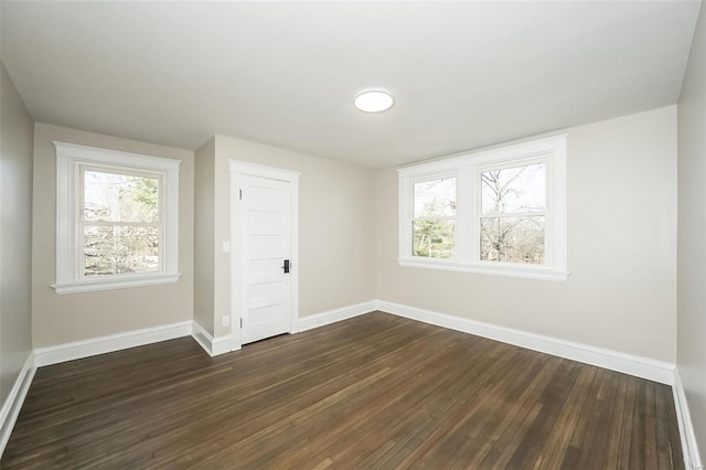 unfurnished room featuring dark wood-style floors, a wealth of natural light, and baseboards