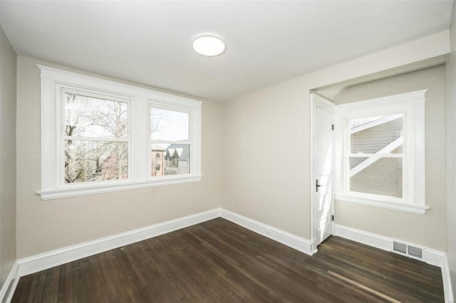 empty room with dark wood-style floors, visible vents, and baseboards