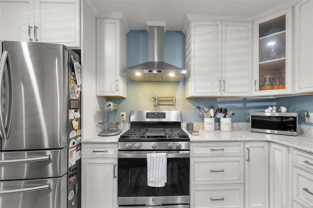 kitchen featuring wall chimney exhaust hood, glass insert cabinets, light stone counters, stainless steel appliances, and white cabinetry