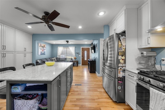 kitchen featuring appliances with stainless steel finishes, light wood-style floors, open floor plan, white cabinetry, and wall chimney exhaust hood