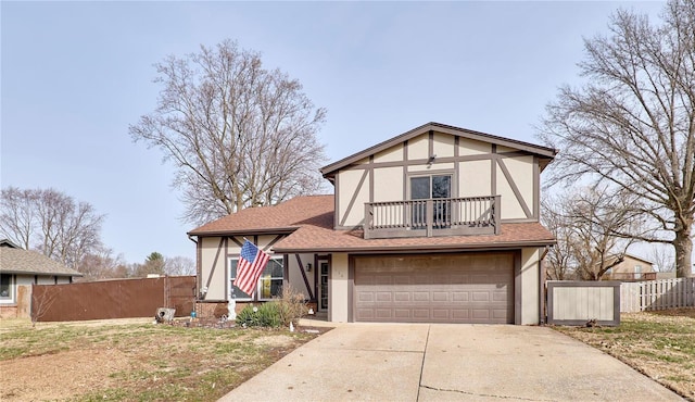 tudor house featuring driveway, a balcony, fence, and stucco siding