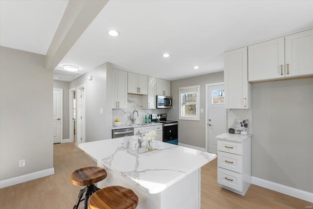 kitchen featuring light stone counters, stainless steel appliances, a sink, baseboards, and light wood-type flooring