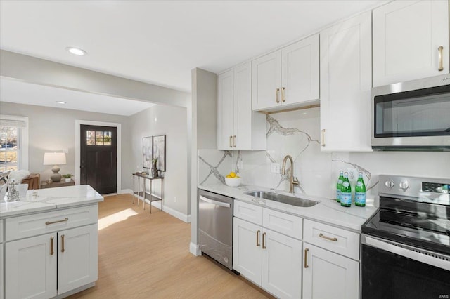 kitchen with decorative backsplash, appliances with stainless steel finishes, light wood-style floors, white cabinetry, and a sink