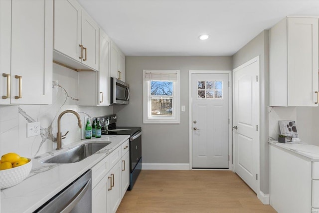 kitchen with white cabinets, appliances with stainless steel finishes, a sink, light wood-type flooring, and backsplash