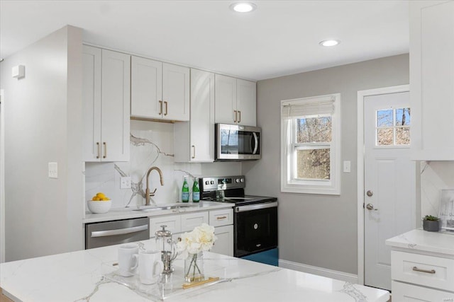 kitchen with stainless steel appliances, decorative backsplash, white cabinets, a sink, and light stone countertops