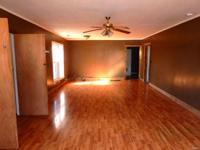 empty room with ceiling fan, baseboards, wood finished floors, and crown molding