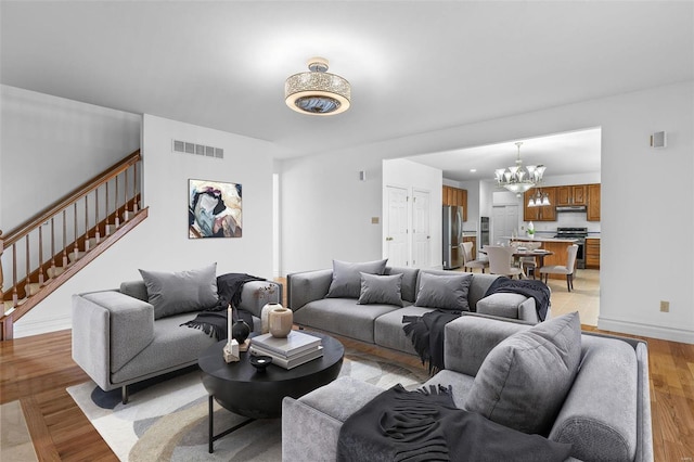 living area featuring light wood-style flooring, a notable chandelier, visible vents, baseboards, and stairway