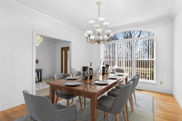 dining space featuring light wood-style floors, crown molding, a notable chandelier, and baseboards