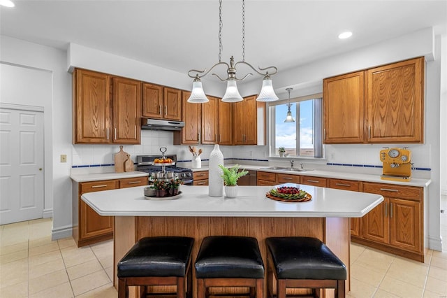 kitchen with light countertops, brown cabinets, stainless steel range with gas cooktop, and under cabinet range hood