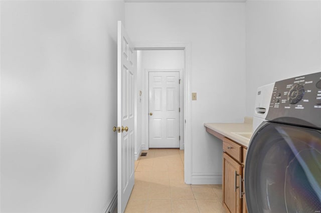 clothes washing area featuring washer / dryer, light tile patterned floors, baseboards, and cabinet space