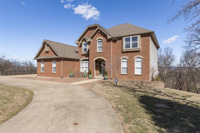 view of front of property with driveway, roof with shingles, a front yard, and brick siding