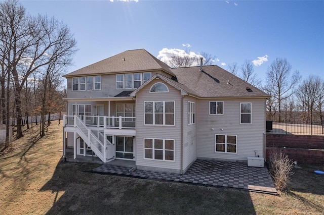 rear view of house featuring roof with shingles, a patio, a lawn, fence, and stairs