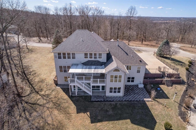 back of house featuring roof with shingles, stairs, a patio, and a yard