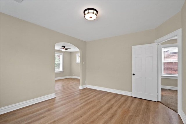 empty room featuring arched walkways, light wood-type flooring, and baseboards