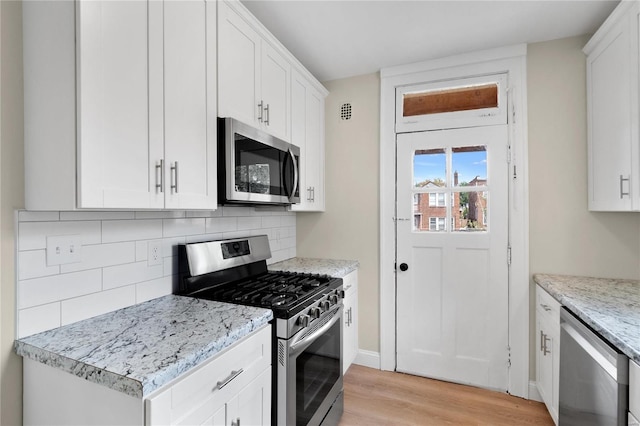 kitchen featuring light wood finished floors, tasteful backsplash, white cabinets, light stone countertops, and stainless steel appliances