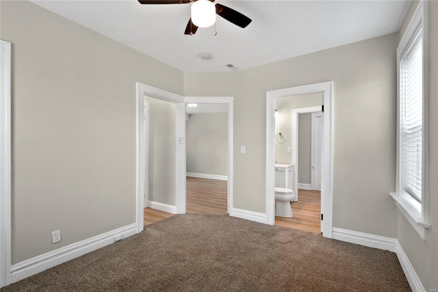 unfurnished bedroom with carpet, connected bathroom, baseboards, and ceiling fan