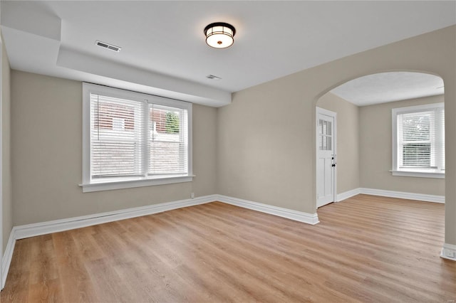 unfurnished room featuring arched walkways, light wood finished floors, visible vents, and baseboards