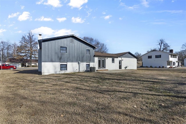 back of house featuring a patio, brick siding, a lawn, board and batten siding, and a chimney