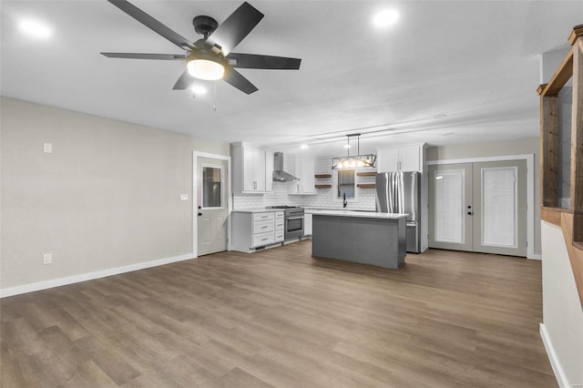 kitchen featuring wood finished floors, a kitchen island, light countertops, appliances with stainless steel finishes, and wall chimney exhaust hood