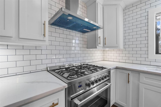 kitchen featuring light stone counters, decorative backsplash, white cabinetry, high end stove, and wall chimney exhaust hood