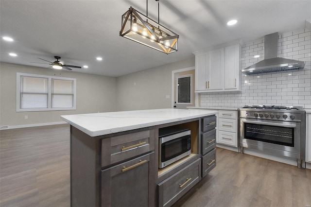 kitchen featuring tasteful backsplash, white cabinets, dark wood-style floors, appliances with stainless steel finishes, and wall chimney range hood